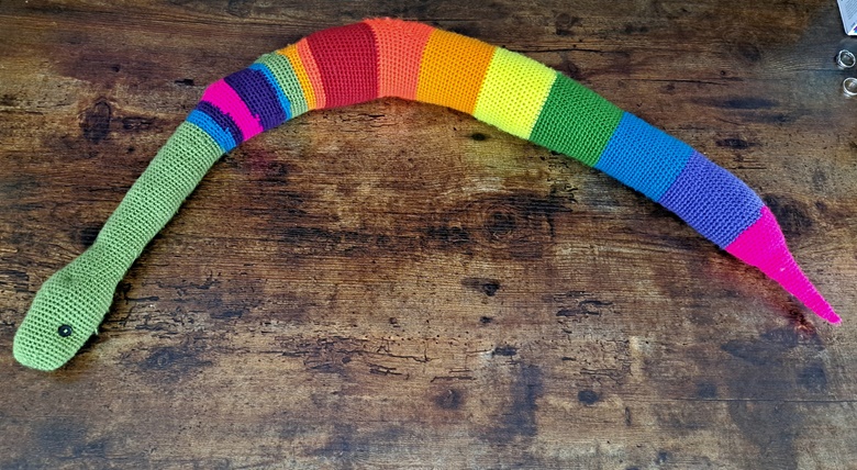 A cute artisan-made rainbow striped crocheted snake pet toy on a wood floor