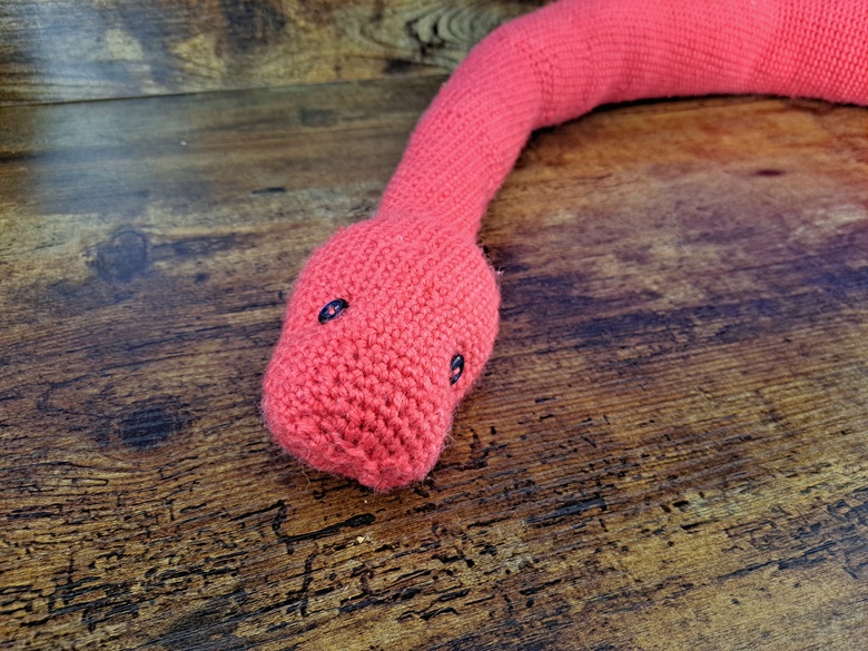 A cute artisan-made pink crocheted snake pet toy on a wood floor