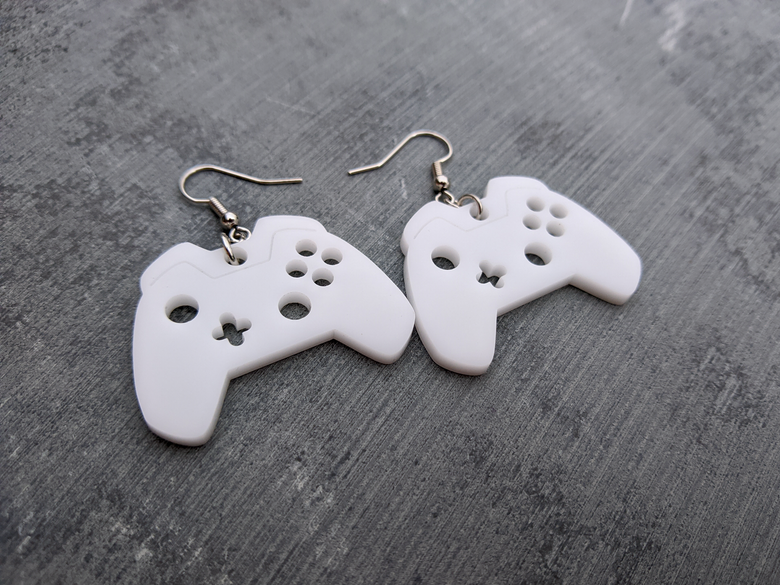 A pair of flat, white dangly earrings inspired by a modern gam controller.
