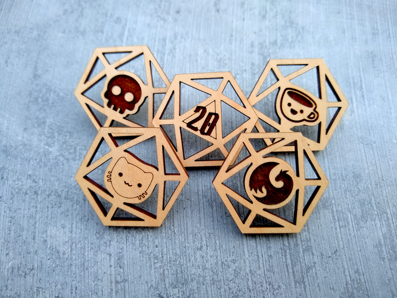 A set of 5 wooden laser cut pins in the shape of d20 dice. Each has a different face: a cat, a skull, a 20, a dragon, and a grinning coffee mug.