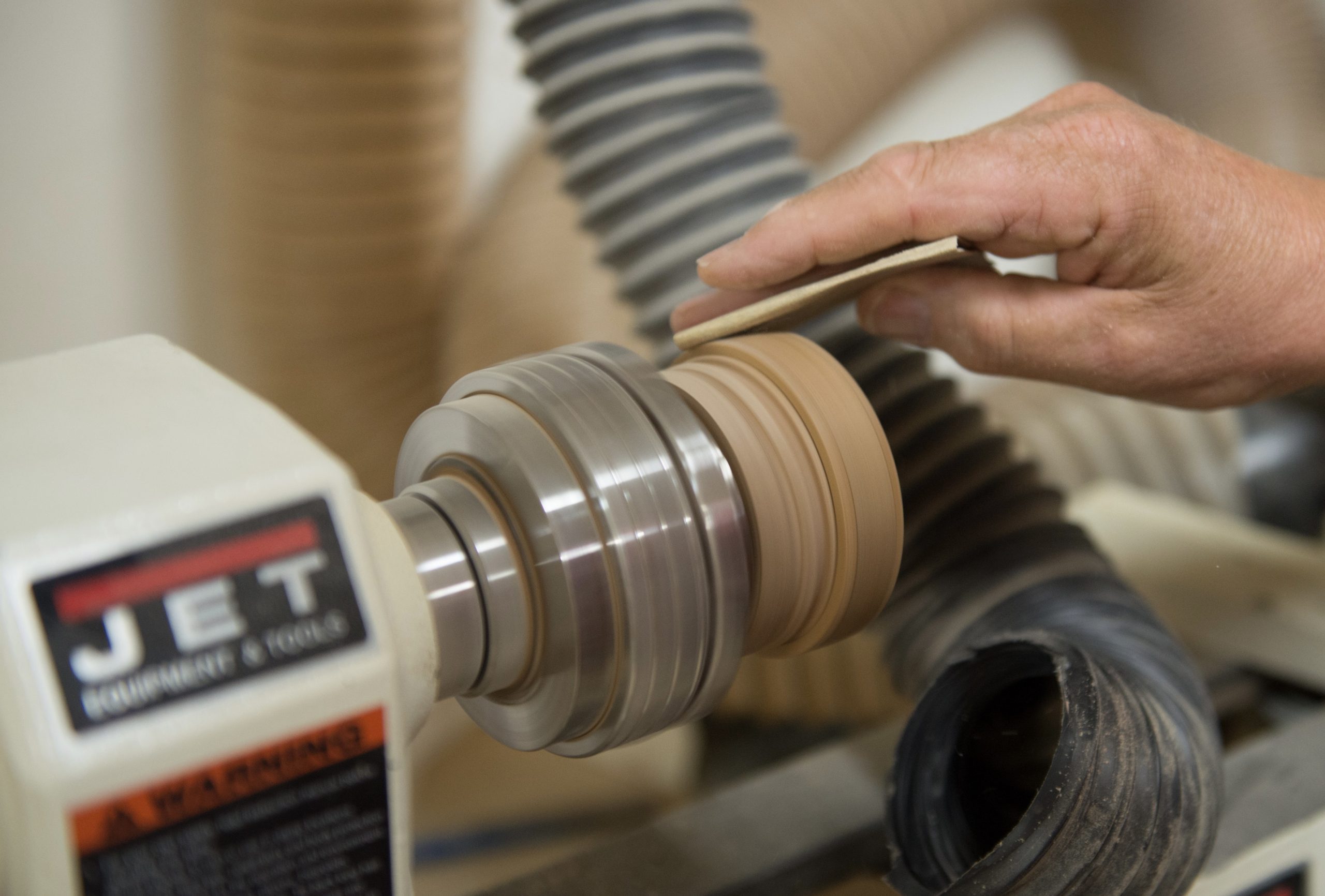 A senior maker's hand holding wood to a sander lathe in a woodcrafting workshop Credit Schuttenworks