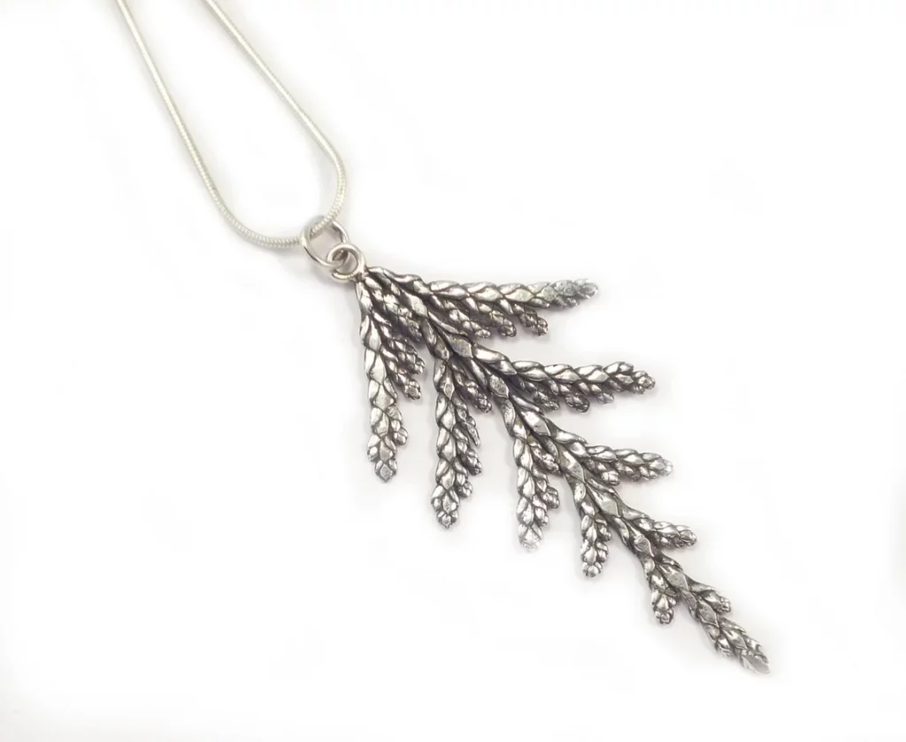 A photo of a silver cedar branch necklace angled on a white background. The necklace chain disappears out of top left frame.