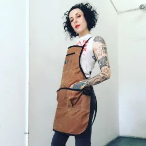 Tough-looking woman with tattoos on her arms wearing a duck canvas Carthartt like apron