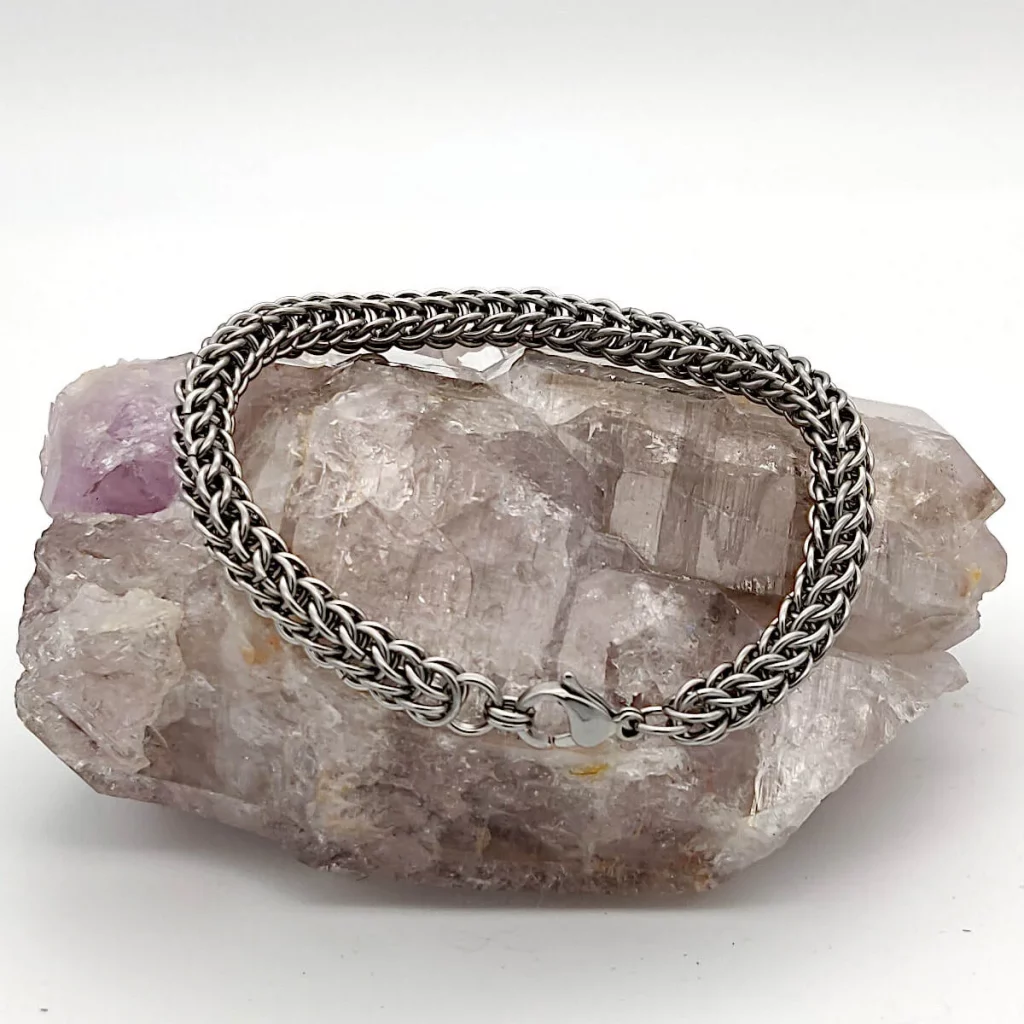 Close-up photo of a silver chainmaille bracelet handmade with a lobster clasp. The bracelet was handmade by Noctua Designs and it is sitting on a natural  rock geode. 