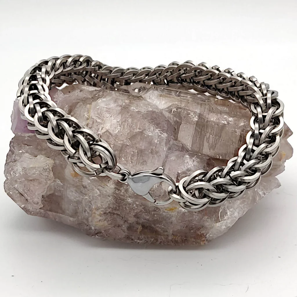 Close-up photo of a silver chainmaille bracelet handmade with a lobster clasp. The bracelet was handmade by Noctua Designs and it is sitting on a natural  rock geode. 