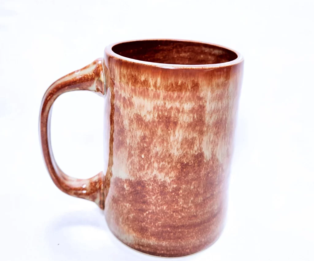 Picture of reddish brown handmade pottery mug with handle on white background.