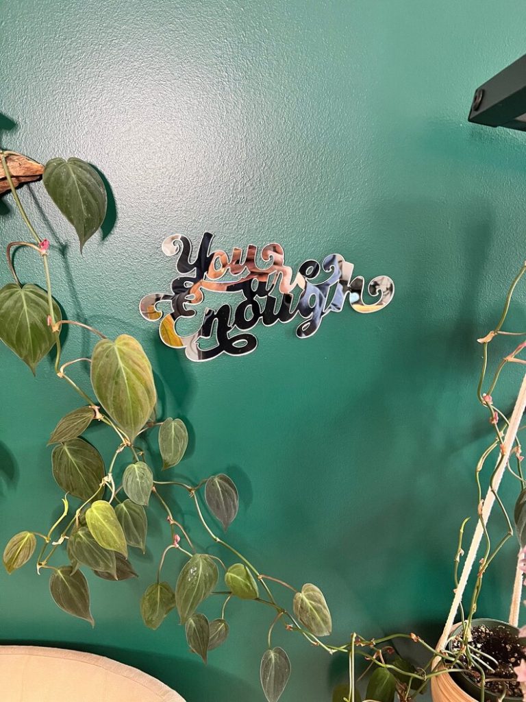 Picture of handmade "You are enough" mirror hanging on a green wall.