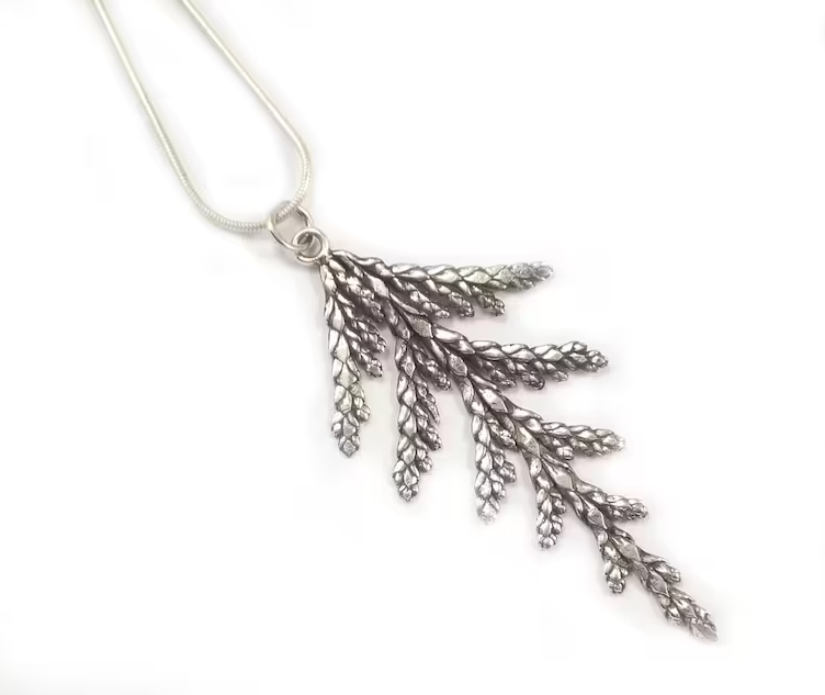 Photo of handmade sterling silver necklace. The necklace is in the shape of a sprig from a cedar tree. The necklace is sitting on a white background.