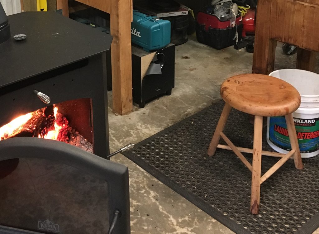 Handcrafted 3-legged stool in a workshop in front of a roaring wood stove. Photo by Walnut Studiolo
