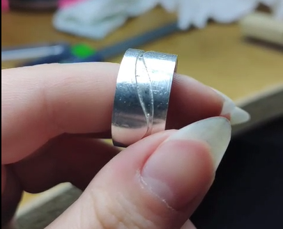 Handmade metal ring with a small wave design, sitting on a finger, showing the camera. Made by hand by Tyler.
