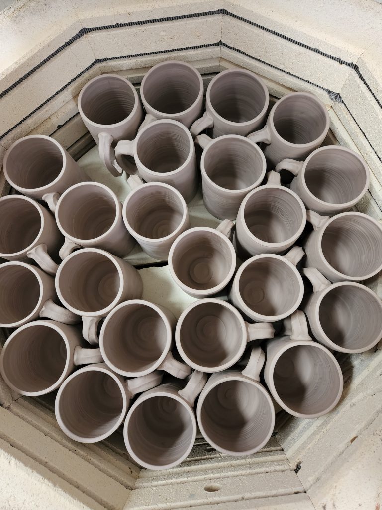 A top-down photo of a many pottery mugs sitting in a kiln. 