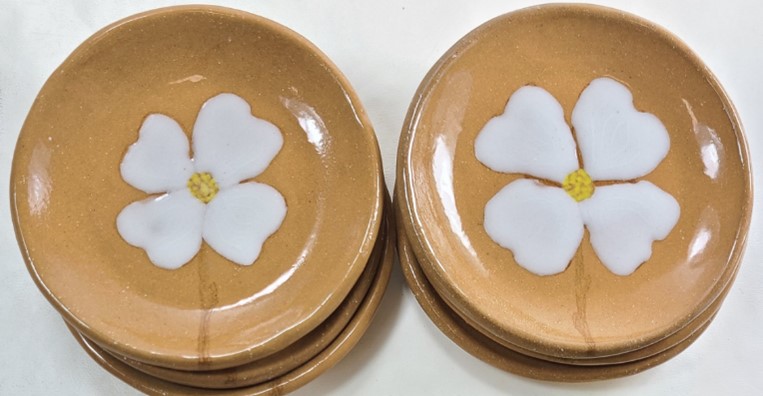 Two stacks of brown-yellow plates with painted white dogwood flowers in the centers.