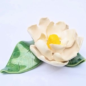 A sculpture of a white magnolia flower with two green leaves. 