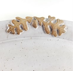 A photo off the edge of a speckled white plate with two oak leaves and acorn molded on the edge.