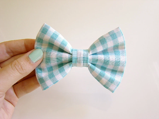A photo of a hand holding a blue and white plaid bowtie