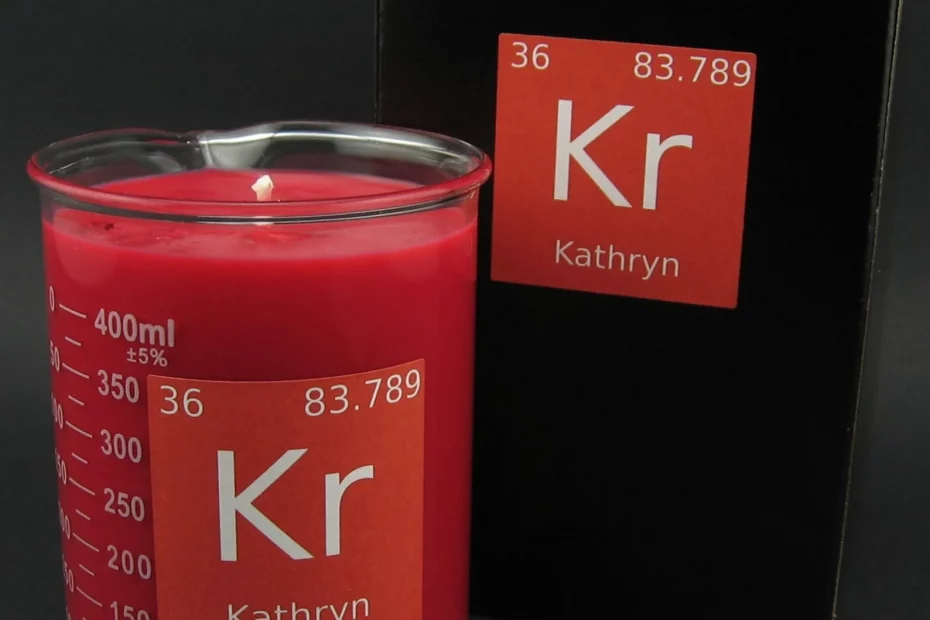Pink candle in a beaker with a rectangular label that looks like a periodic table entry but reads "Kathryn KR" sits in front of a slightly larger box.