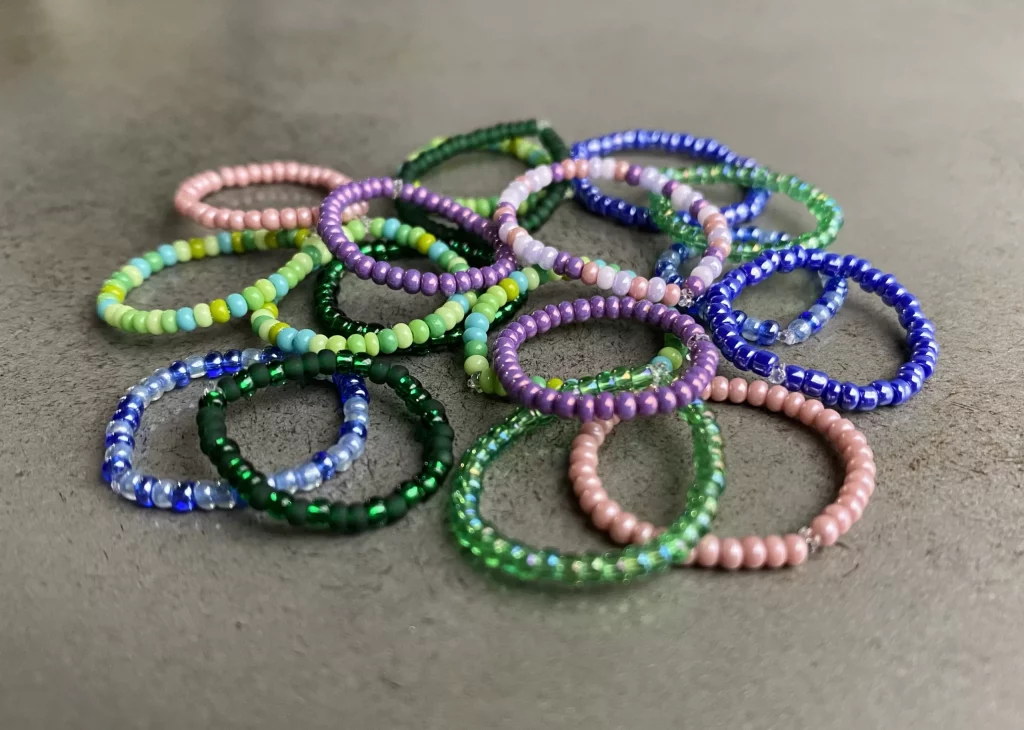 A pile of rings made with blue, purple, green and rose beads. 