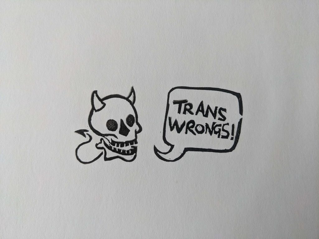 An illustration of a skull with devil horns and a tail, with a speech bubble that says, "TRANS WRONGS!"