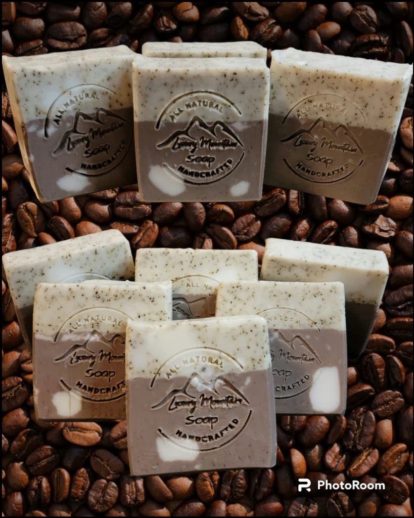 Soap bars sit atop coffee beans. Each one is half coffee colored and half cookies and cream colored. All are stamped with Luxury Mountain Soap's logo.