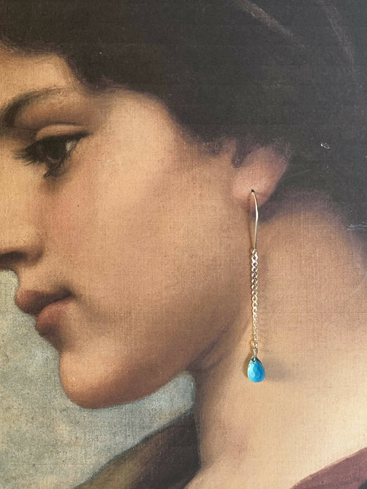 A photograph of a woman's renaissance style portrait has a real earring dangling from her ear. It is one single long chain with a turquoise tear drop at the end.