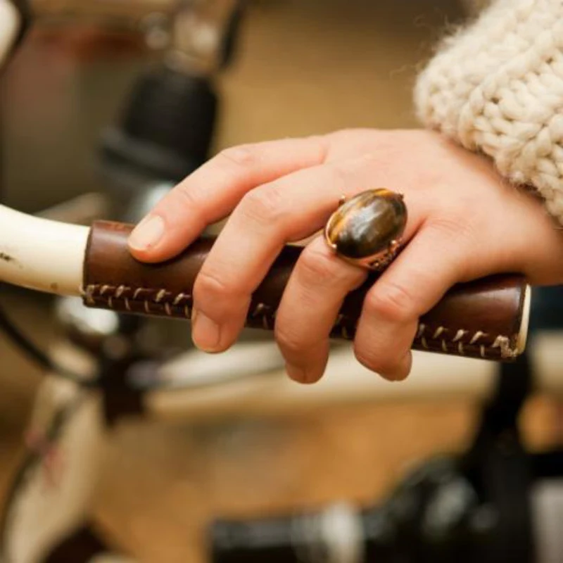 A hand resting on a handmade leather bicycle grip made from a reused section of hide