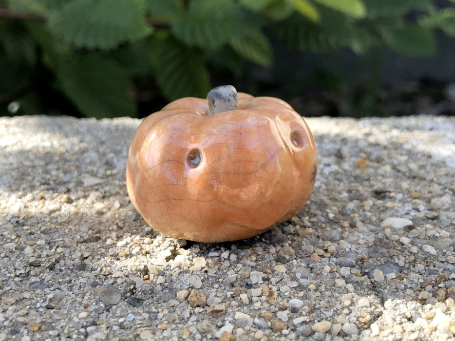Small orange stoneware pumpkin sculpture. Speckled light falls over the little guy. It looks like it's smiling.