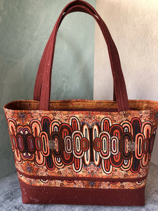 A handmade structured tote bag with long handles. The fabric is red-brown, orange, and white with long upright ovals of varying sizes overlapping each other around the center.