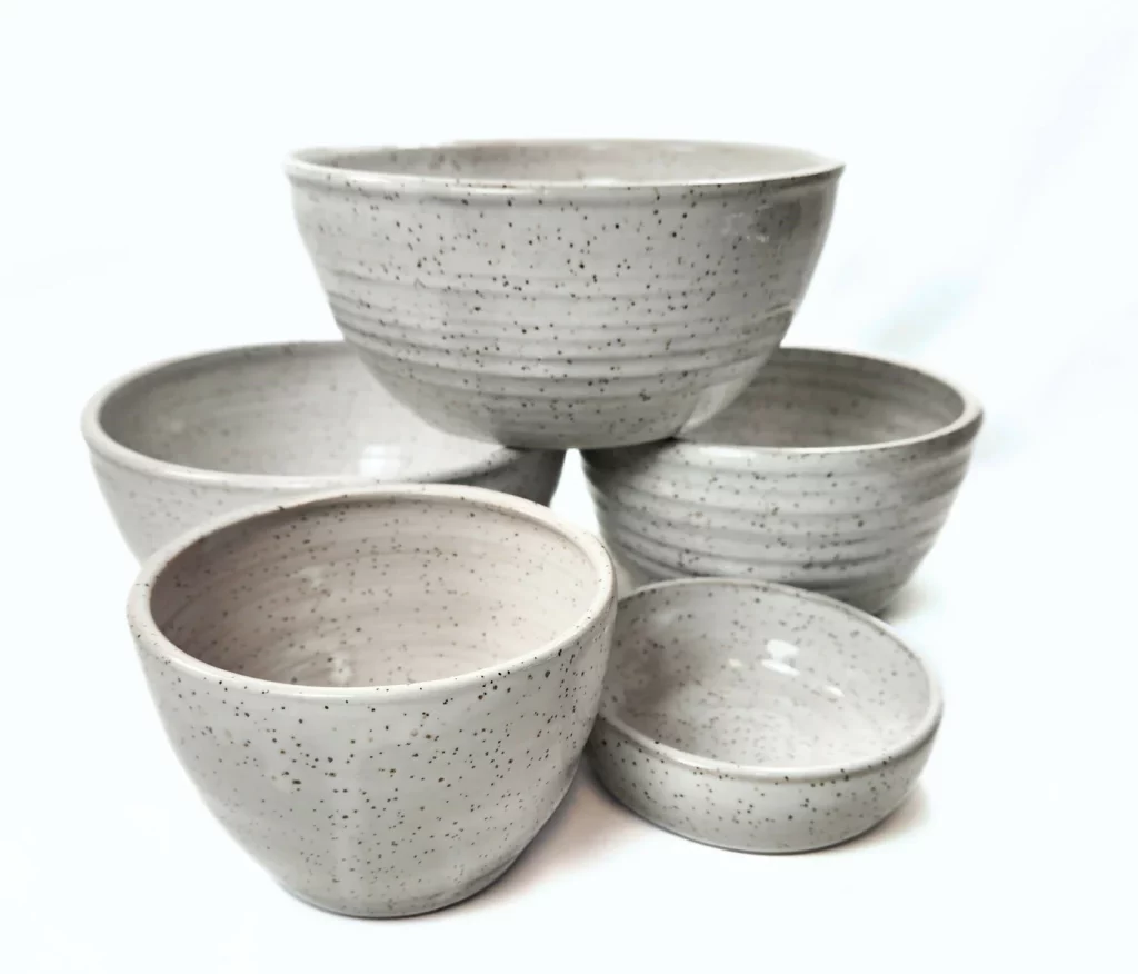A stack of speckled white stoneware bowls in varying sizes, hand thrown on the potter's wheel