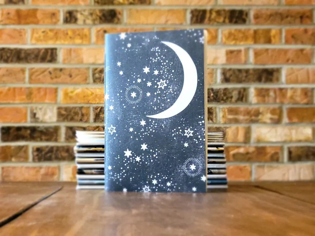 A handmade soft cover sketch book with a moon and stars pattern on the cover in dark blue and light yellow or white