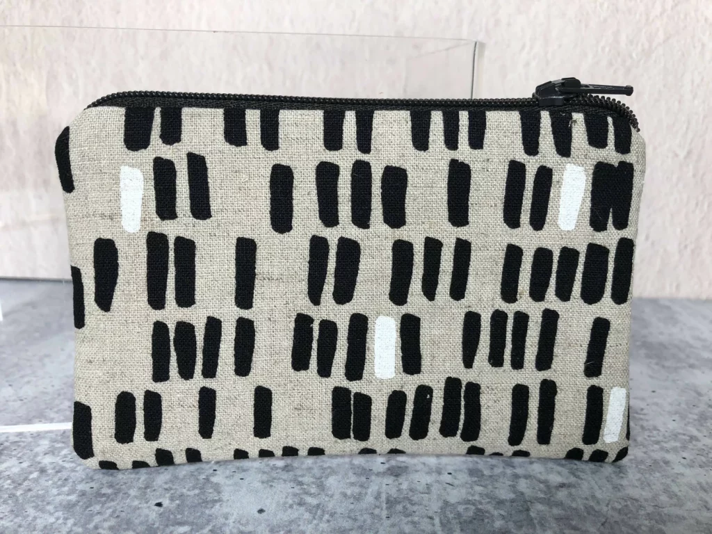 A hand-sewn coin purse with a black and white mod 60s print on a natural jute looking background