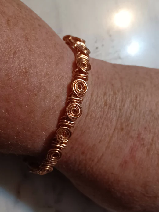A hand is wearing a copper bracelet. The bracelet has intricate swirling wraps of copper around the outside.