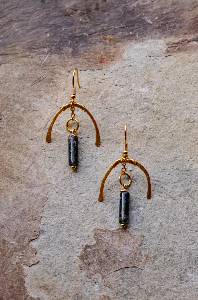 Unique dangling earrings made of copper and a dark blue stone. There is a copper arc like an umbrella on top of a the stone which is like an obelisk, a faceted rod