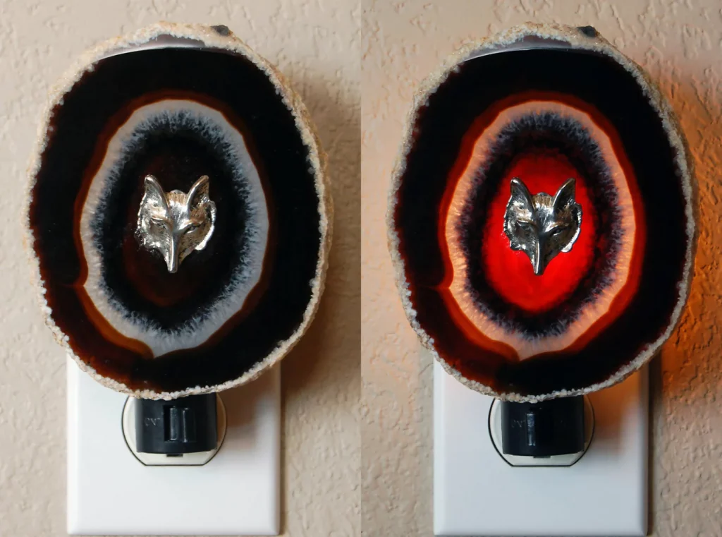 A night light in a socket with a decorative round geode slice for transclucent color in blue and red and a charm of a silver wolf head on top