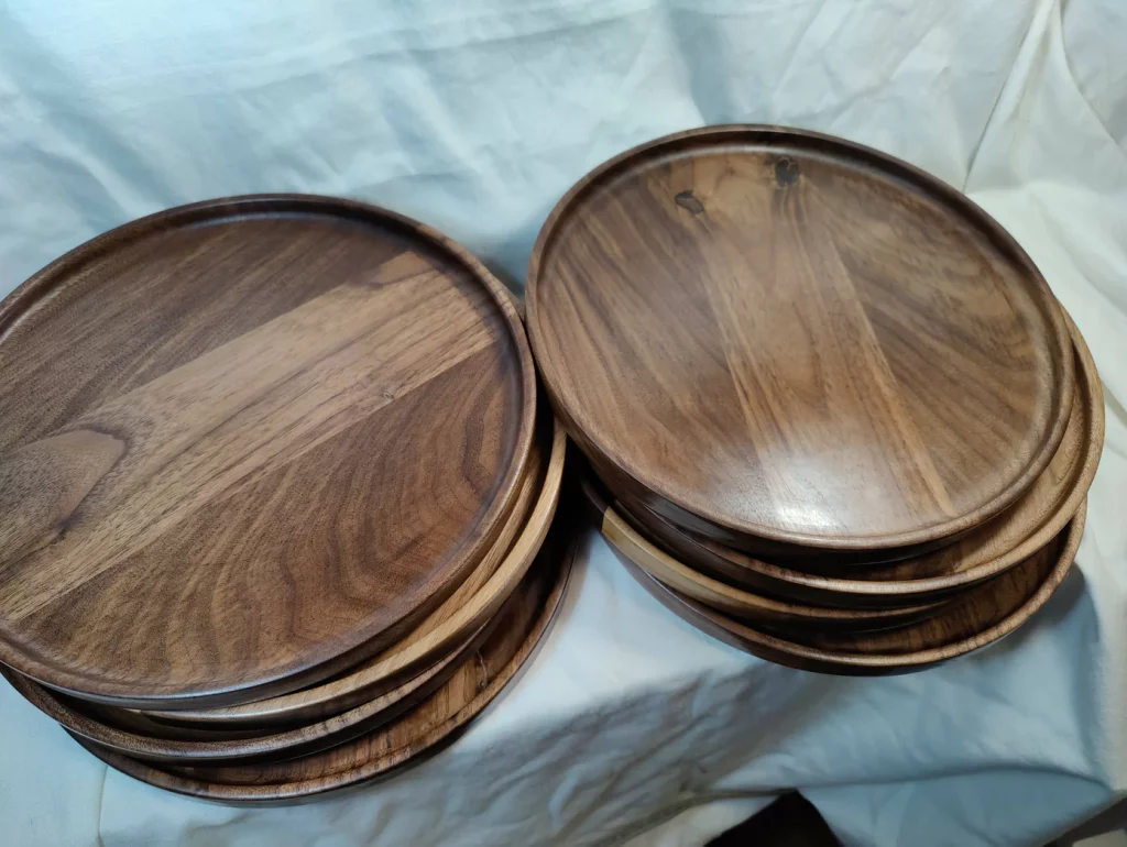 A stack of round dark walnut wood dinner plates, glossy and new