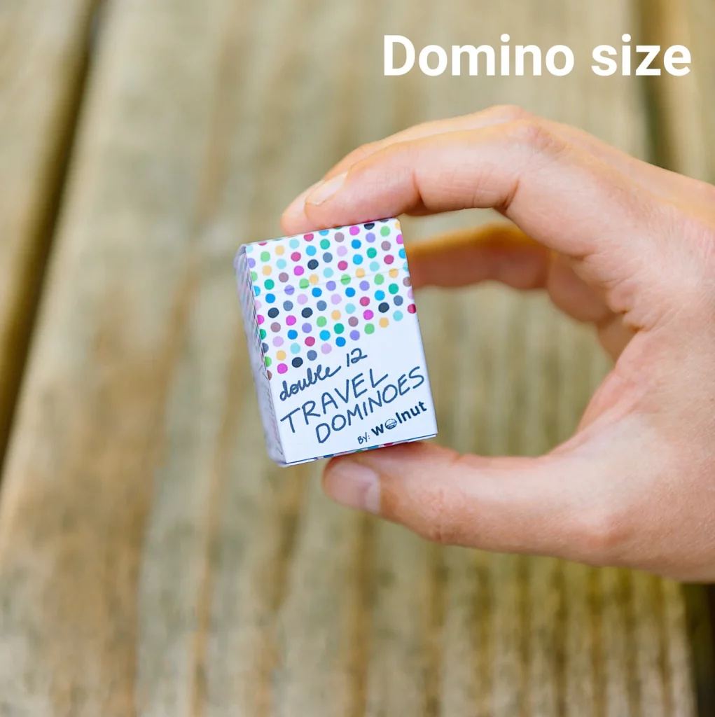 A hand holding a small set of travel sized domino playing cards that are hand drawn and have colorful pips and dots