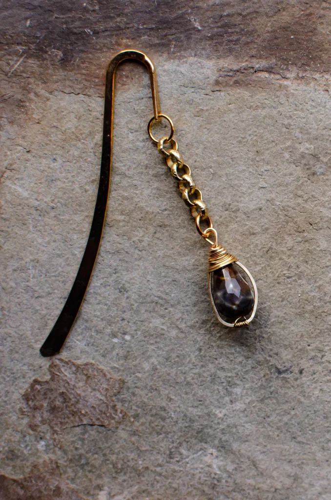 A long metal hook designed to mark the pages in the book with a dangling chain made from copper with an elegant egg-shaped stone at the end