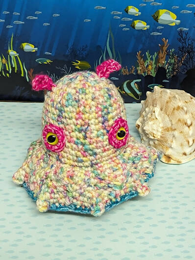 A rainbow yarn crochet octopus with bright pink eyes and "ears"