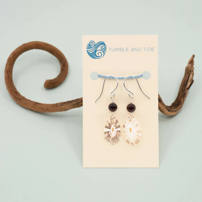 Two garnet and sea shell drop earrings hang from a gift card backing that rests on a swirly piece of driftwood