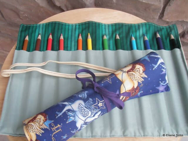 A pencil holder laid out full of colored pencils. On top is a rolled up version of the holder with unicorns on it.