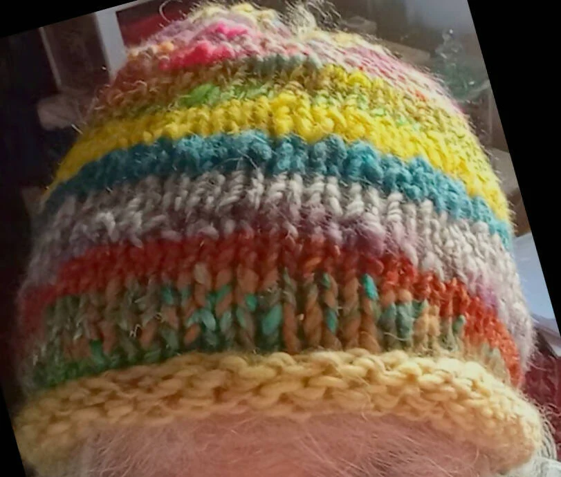 Looking down at a hand knit hat on someone's head. The hat is made of bright layers of colors.