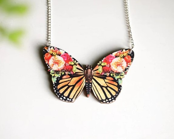 A butterfly wood pendant on a white background with flowers decorating the top two wings.