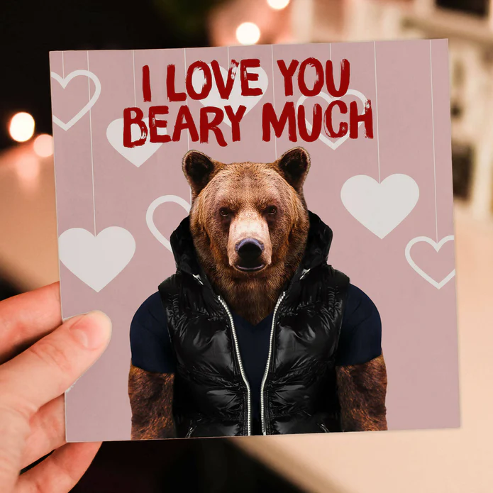 A square, pink card shows a Grizzly bear wearing a black puffy vest jacket with text above him that reads "I love you Beary much" in red.