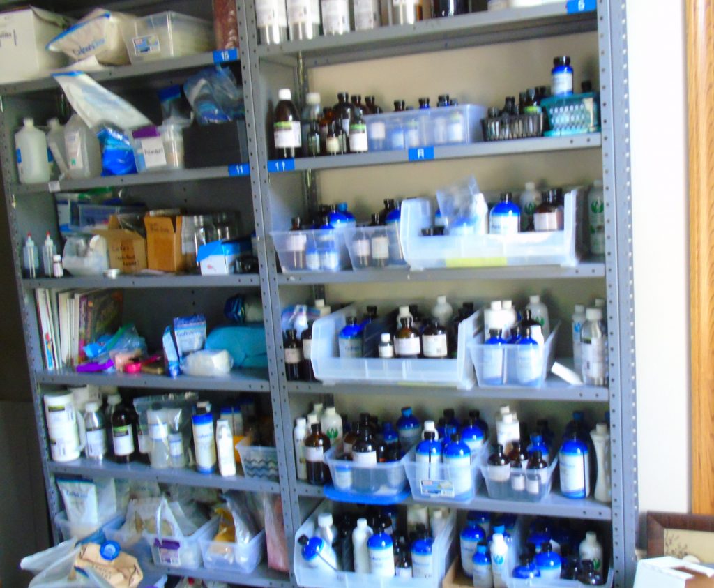 Organized storage shelf of ingredients and essential oils and fragrances used in handmade soap and cleaning product making at Blue Poppy Bath and Body Works