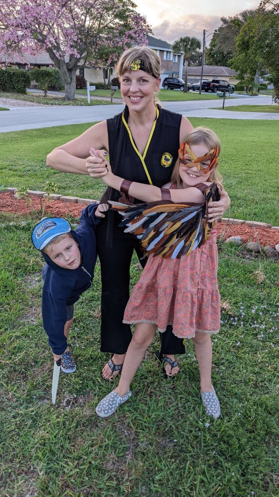Erica Englund of Giddy Hedgehog with her two kids, standing in the yard with their handmade costumes and masks on a pretty spring day in the front yard of a house on a grassy lawn