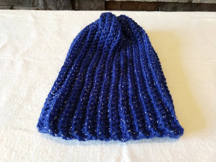 A blue crochet beanie laying flat on a white table.
