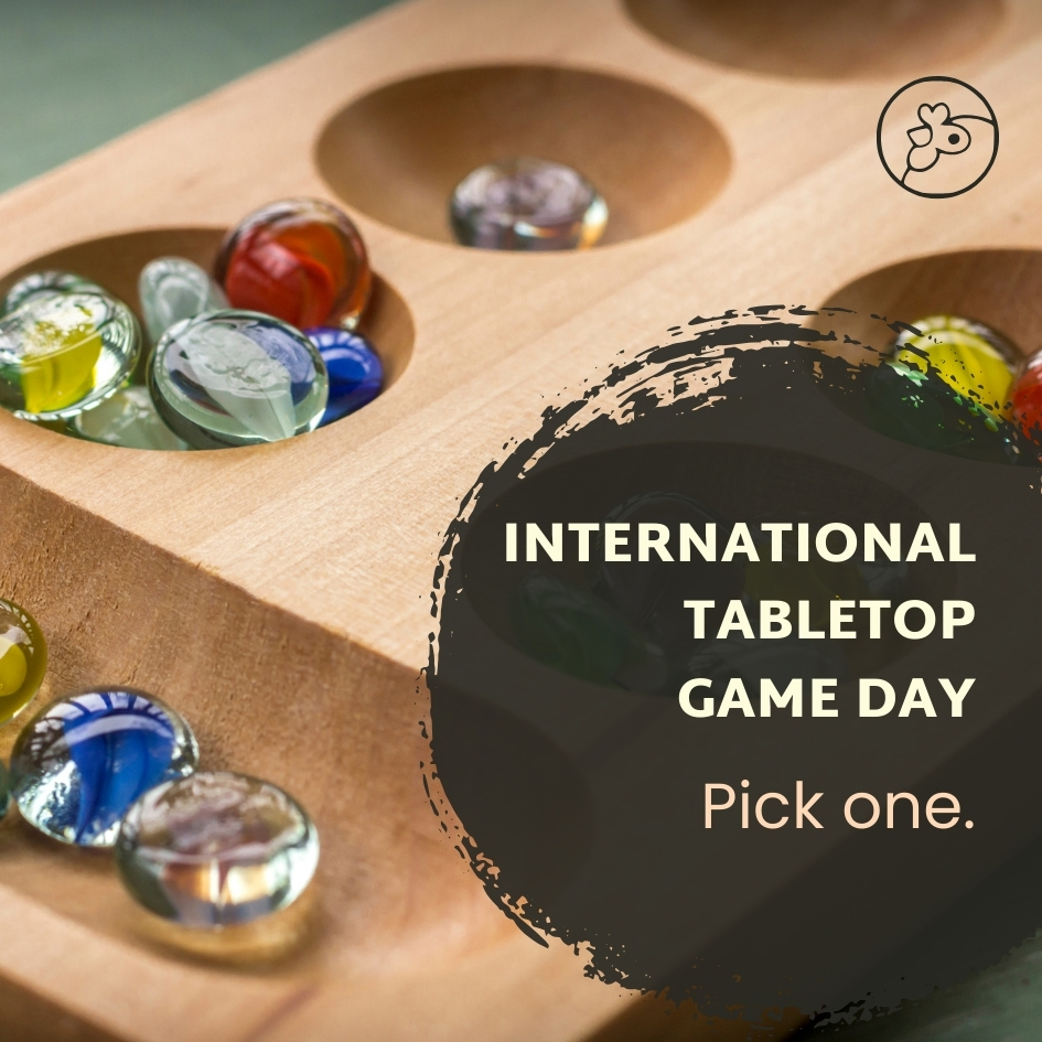 Wooden African game with colorful marbles as counters in depressions while a dark circle and white text that reads International Tabletops Games Day Pick one.