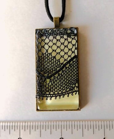A yellow colored rectangular resin pendant covered with traditional silk lace.