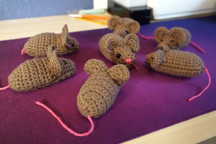A circle of brown crocheted mice on a purple piece of cloth