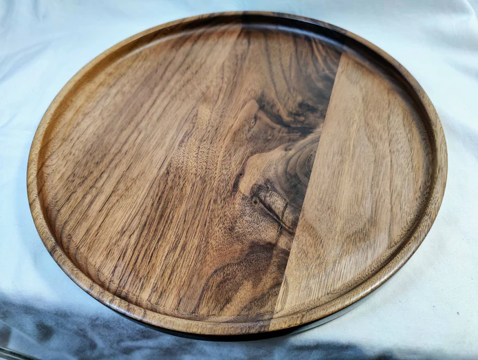 A handmade walnut wooden plate on the edge of a grey table